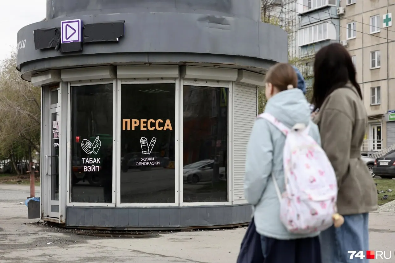 Витрины киоска затонированы, на стеклах появилось «жижи», «одноразки», «табак», а слово «пресса» осталось частично. Мэрия считает павильон самовольным, родители обеспокоены доступностью такой рекламы для школьников.